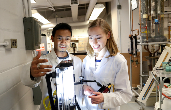 two students in lab coats looking at device